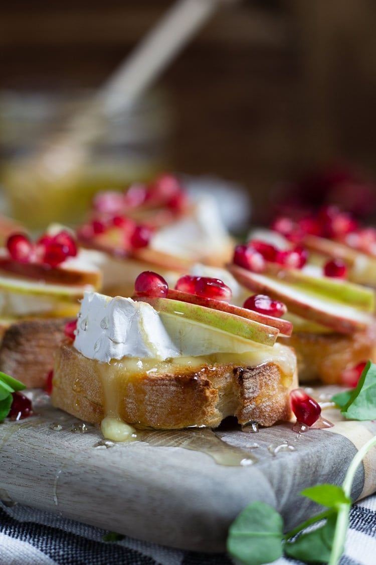 A close up of apple brie crostini garnished with honey and pomegranate seeds