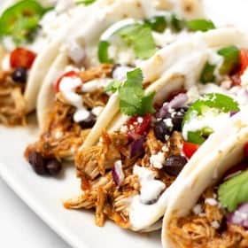 Close up shot of 4 shredded chicken tacos garnished with diced red onion and fresh cilantro