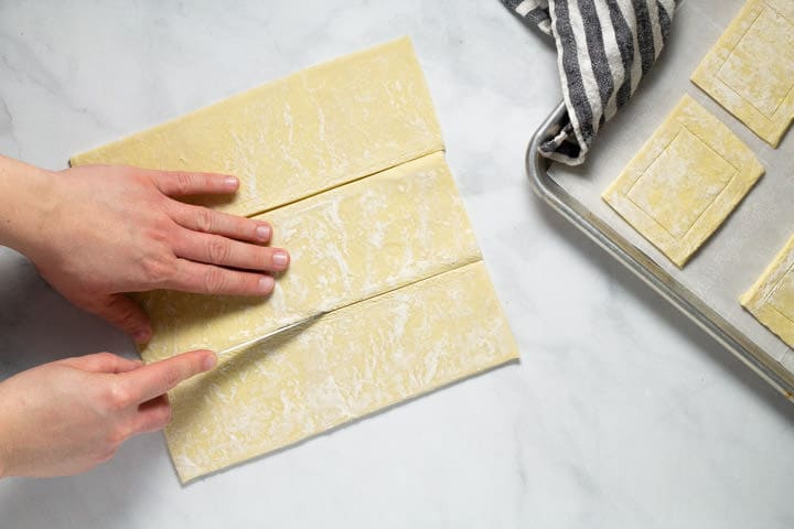 White marble counter top with a sheet of puff pastry being cut into 3 rectangles