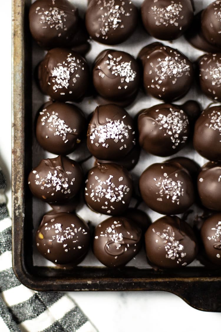 Overhead shot of a baking sheet filled with chocolate covered peanut butter balls garnished with sea salt