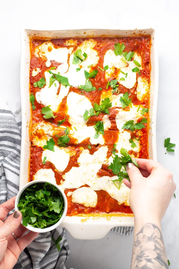 Finished photo of baked manicotti being garnished with fresh chopped parsley