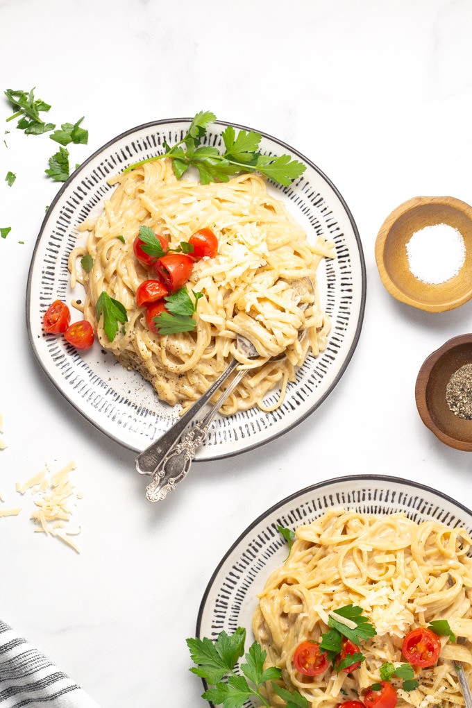 Two plates of fettuccine alfredo garnished with fresh parsley