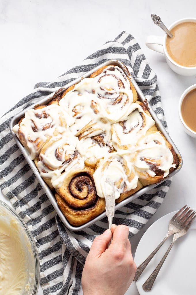 Overhead shot of cinnamon rolls being frosted with cream cheese frosting