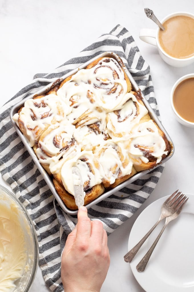 Overhead shot of cinnamon rolls being frosted with cream cheese frosting