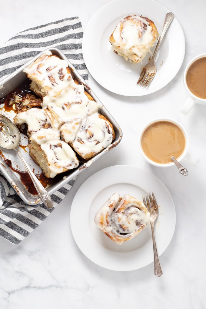 Overhead shot of a table with a pan of cinnamon rolls and two white plates and cups filled with coffee