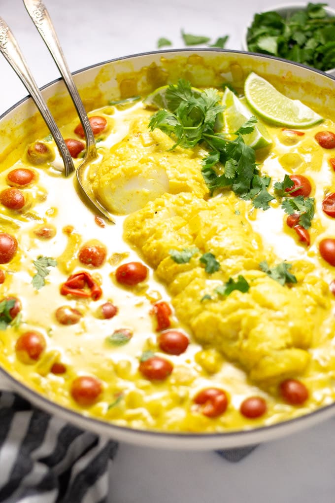Close up shot of a pot filled with tomato coconut curried cod garnished with fresh cilantro