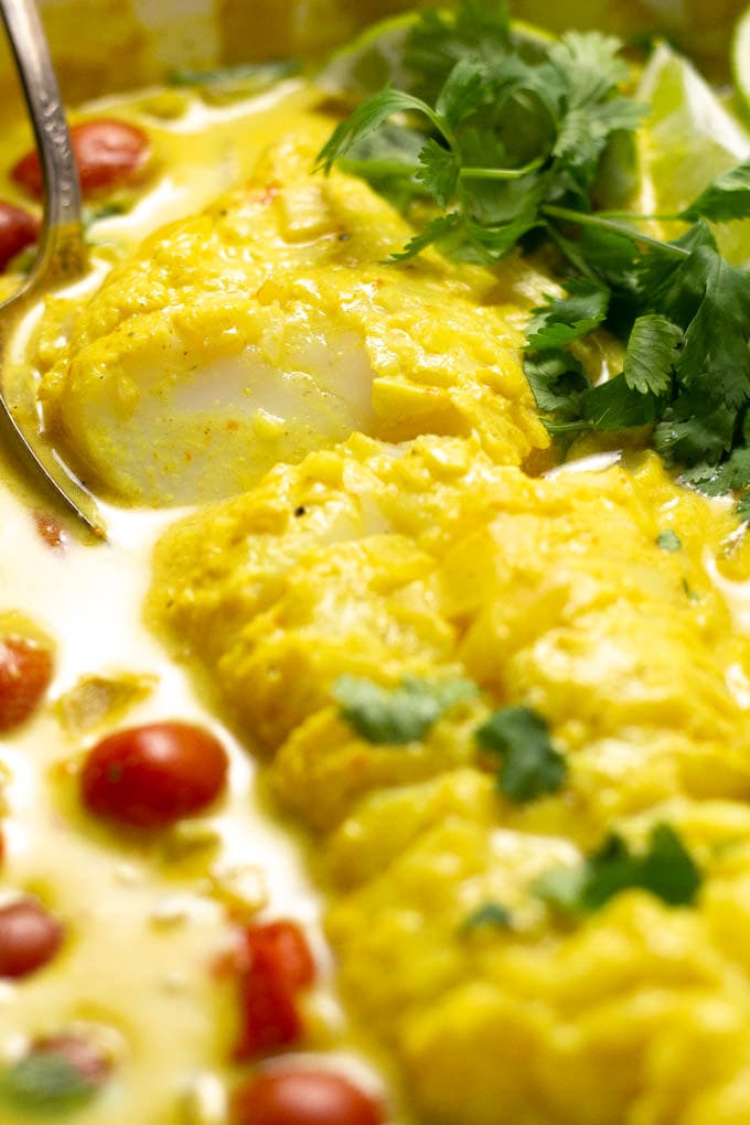 Close up shot of a pot filled with tomato coconut curried cod garnished with fresh cilantro