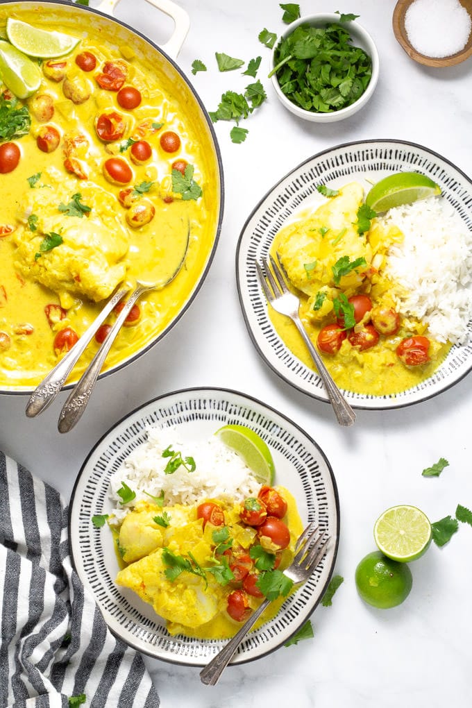 Overhead shot of two plates filled with tomato coconut curried cod garnished with fresh cilantro