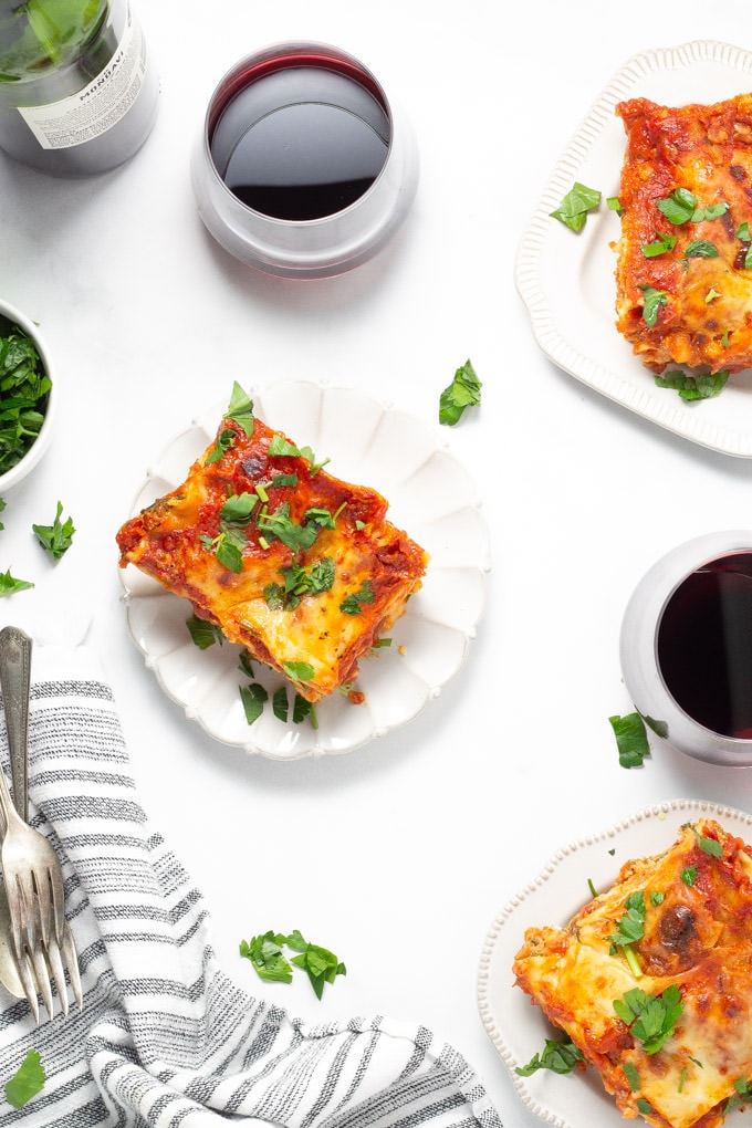 Overhead shot of three slices of lasagna on plates with two glasses of red wine