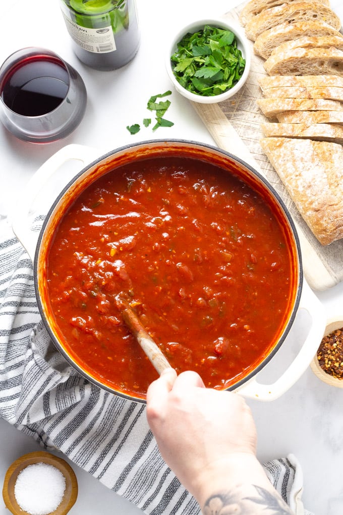 Overhead shot of someone stirring homemade spaghetti sauce in a white pot