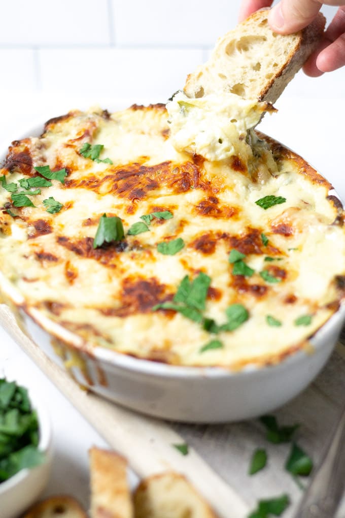 Bread bring dipped into spinach and artichoke dip in a white baking dish