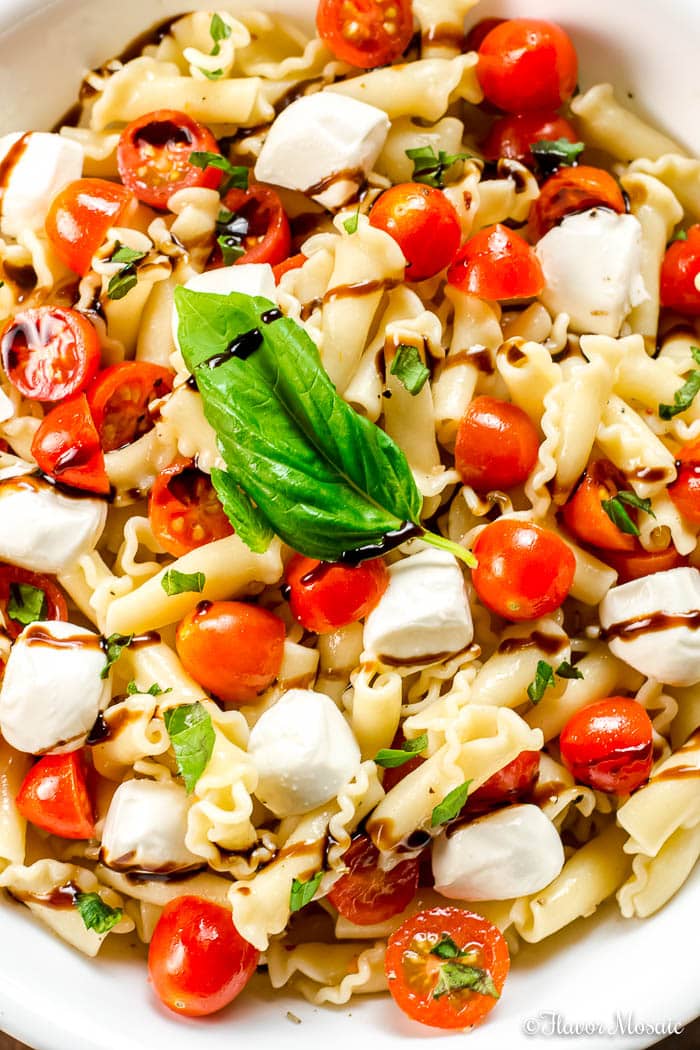 Overhead shot of a white bowl filled with caprese pasta salad drizzled with balsamic reduction