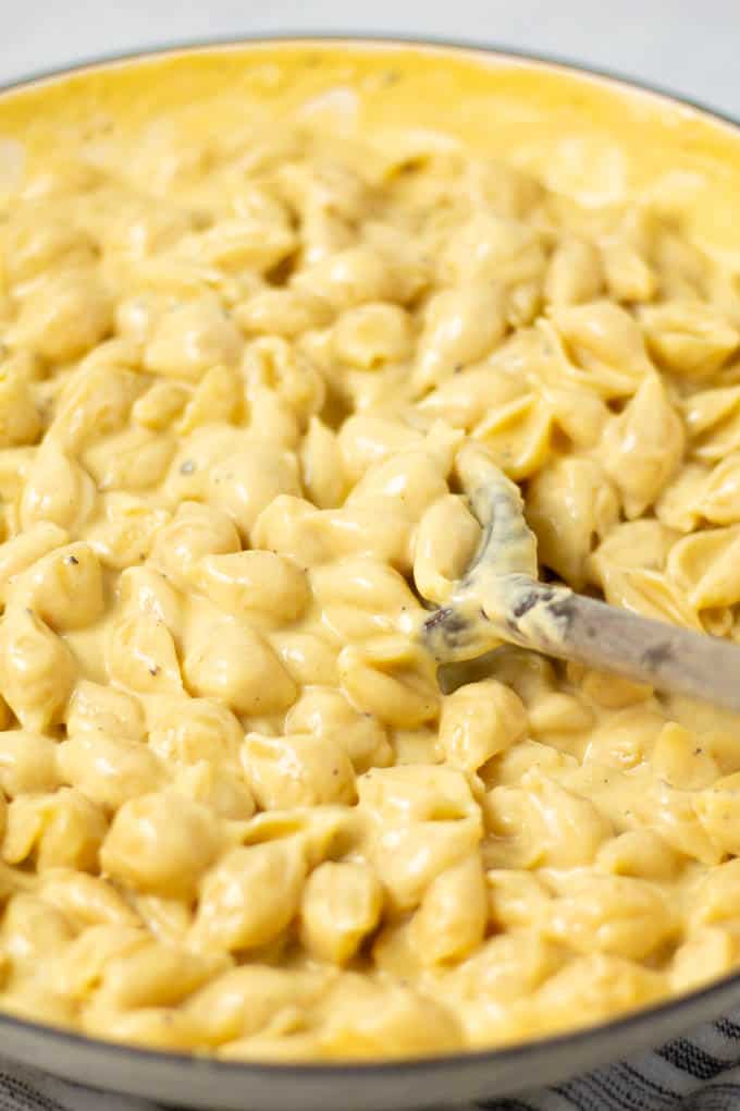 A large pot of mac and cheese being stirred with a wooden spoon