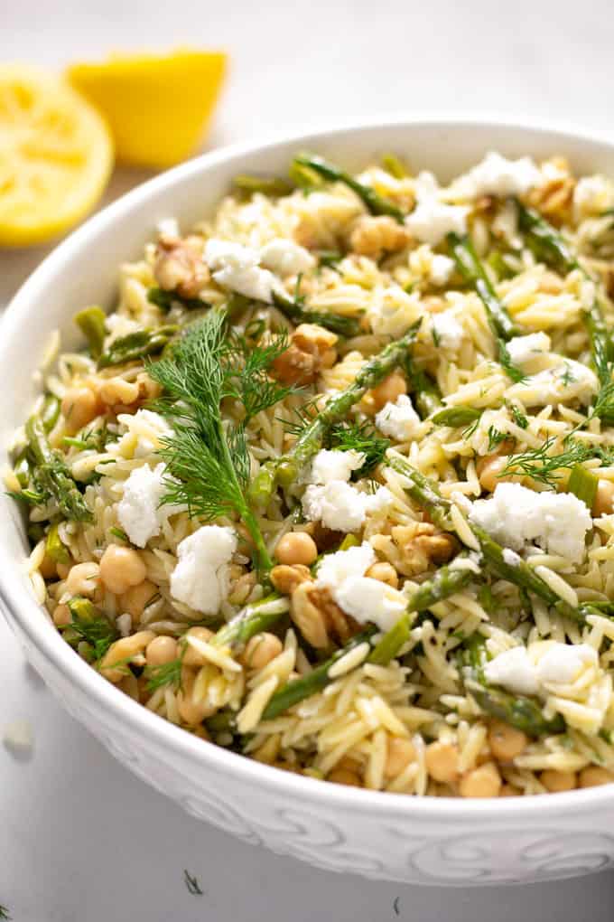 Close up shot of a white bowl filled with pasta salad garnished with fresh dill