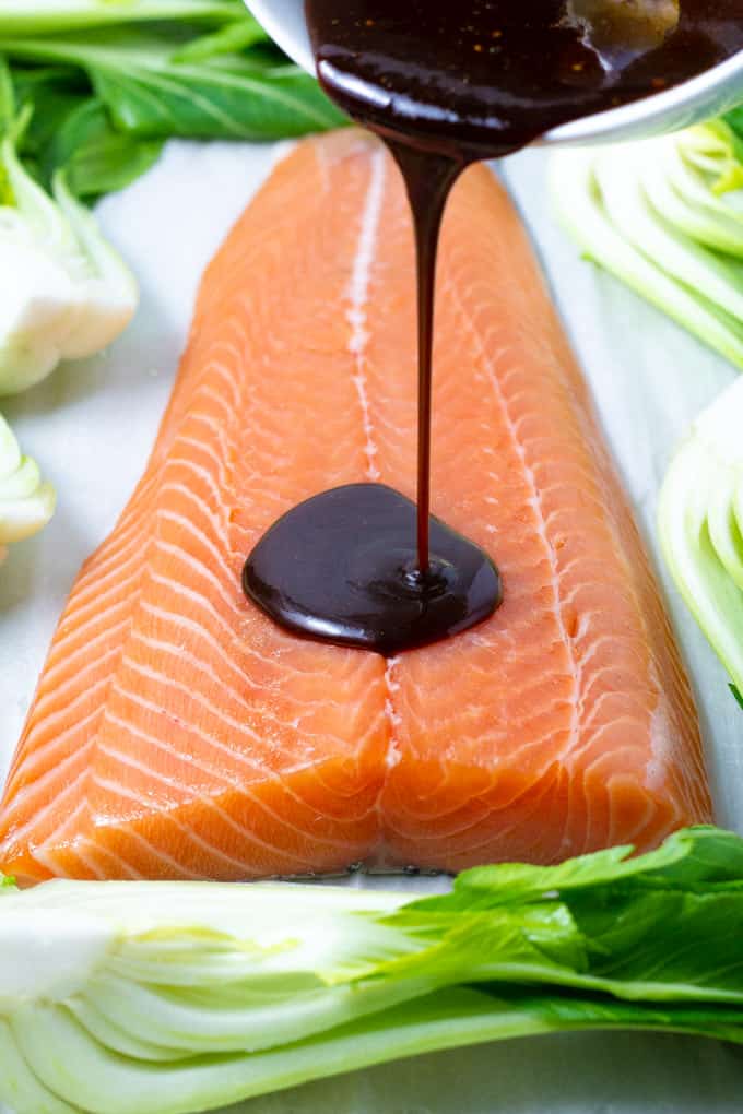 A fillet of salmon on a sheet pan with sauce being poured over it