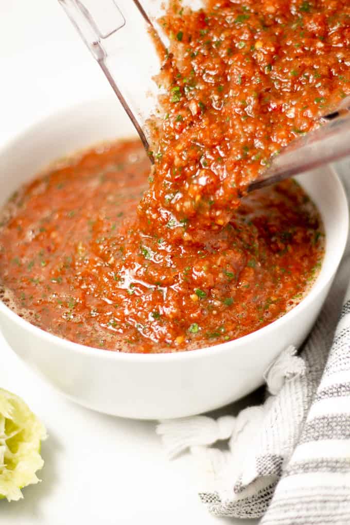 A blender pouring fresh homemade restaurant style salsa into a white bowl