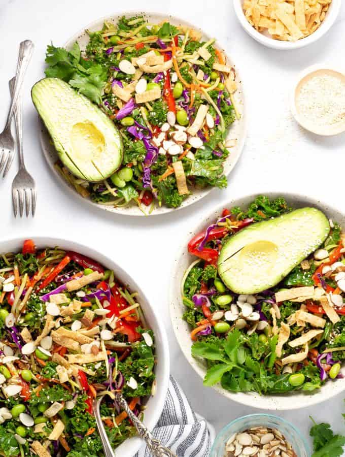 Two plates and a serving bowl of Asian kale salad