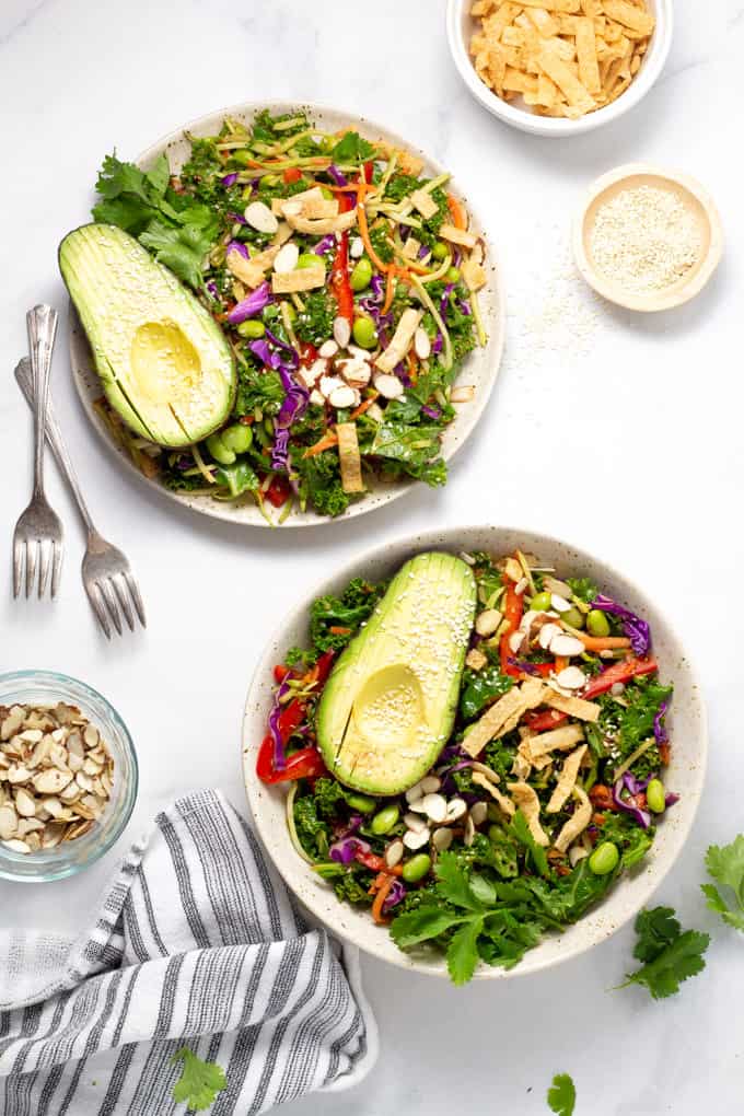 Overhead shot of two bowls and a large serving bowl filled with Asian kale salad