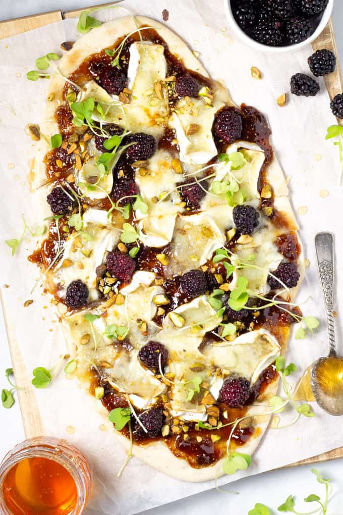 Overhead shot of a brie and blackberry flatbread on a cutting board garnished with microgreens