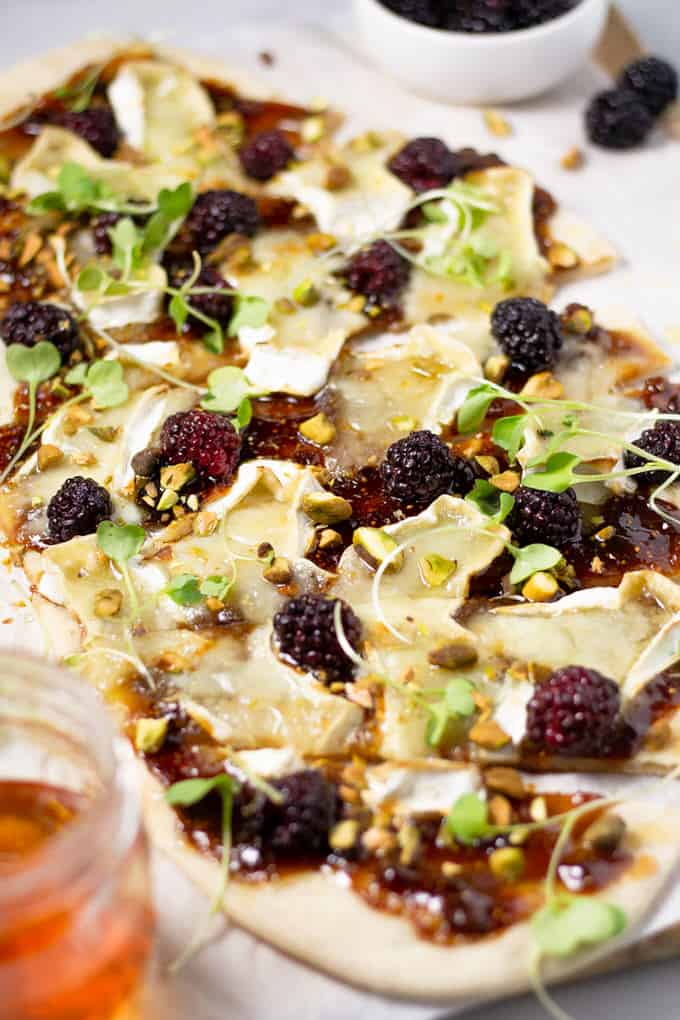 Close up shot of a brie and blackberry flatbread on a cutting board garnished with microgreens