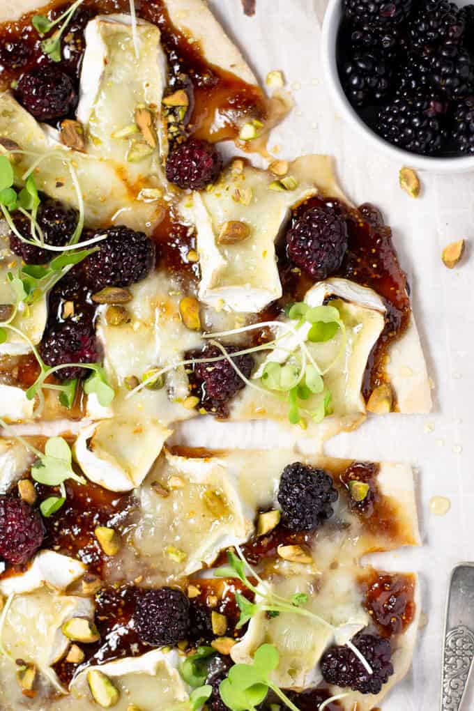 Overhead shot of a brie and blackberry flatbread on a cutting board garnished with microgreens