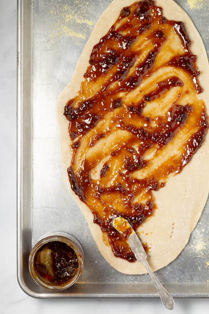 Overhead shot of a flatbread pizza crust on a baking sheet being covered with fig jam