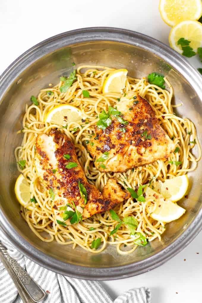 Overhead shot of lemon butter fish with spaghetti in a silver pot garnished with fresh chopped parsley