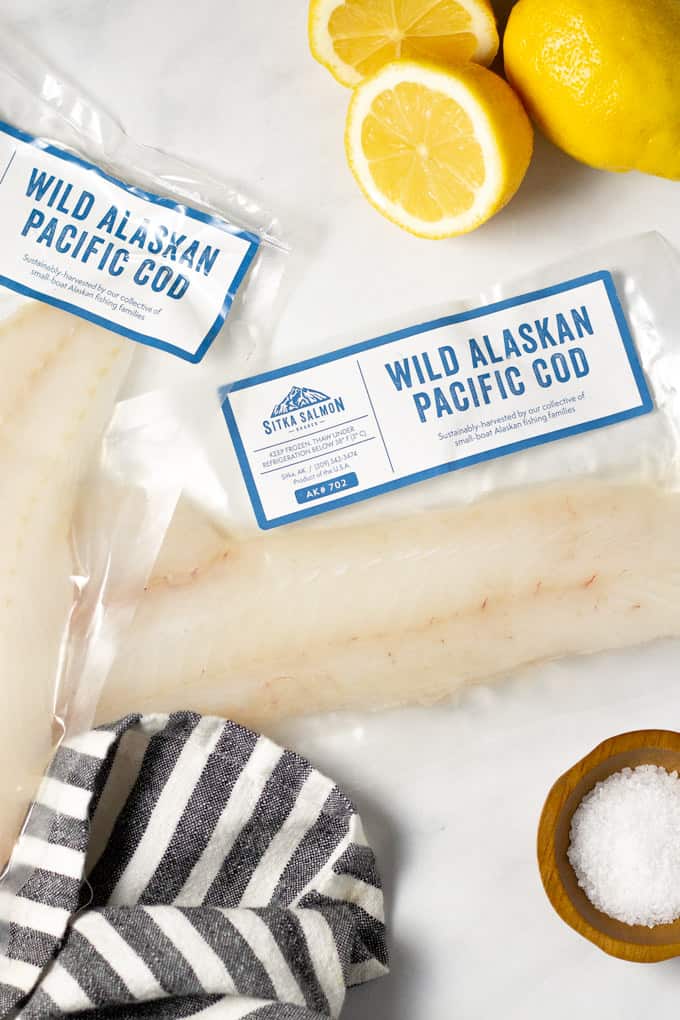 A white marble counter top with two packages of fresh fish and sliced lemons