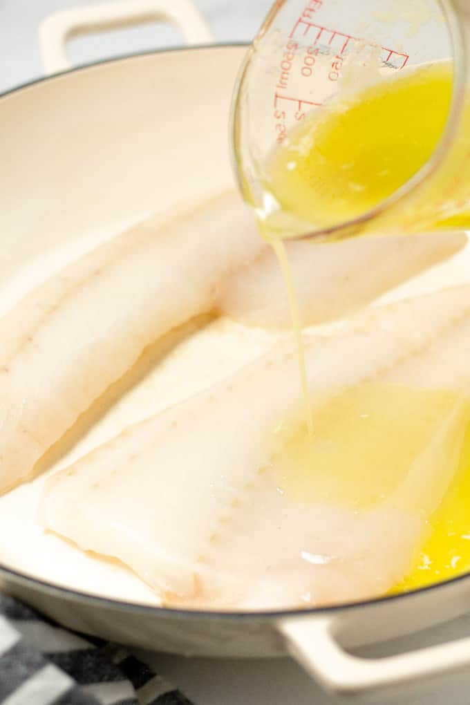 A baking dish with two fish fillets with butter being poured over them
