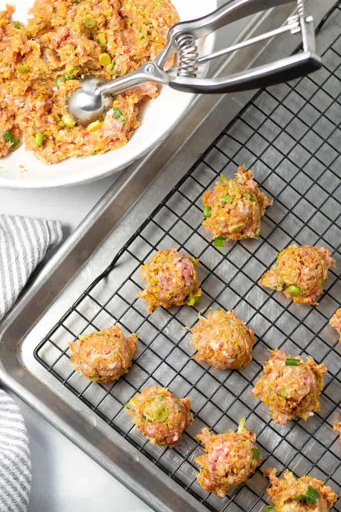Baking sheet with a cooling rack on top and a cookie scoop scooping meatballs