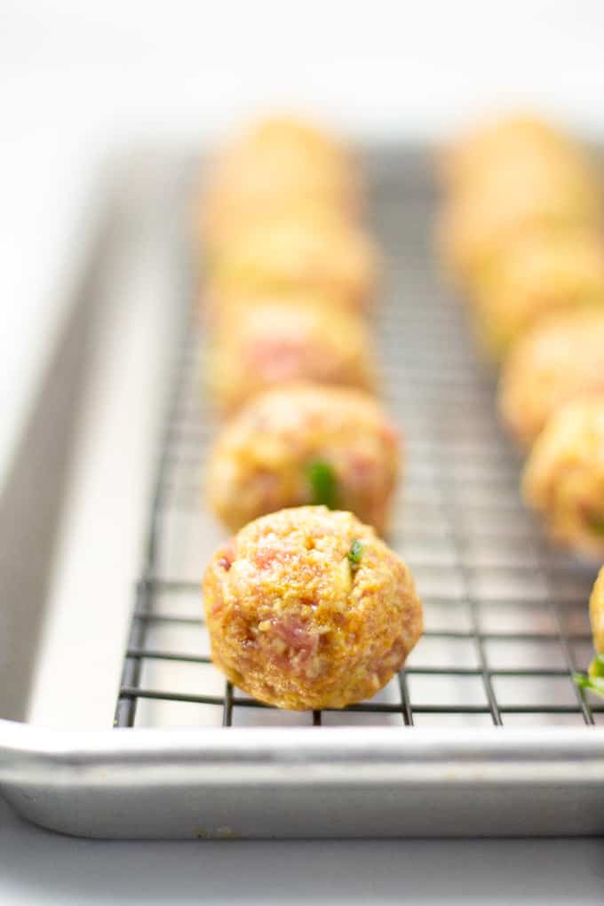 Close up shot of an uncooked pork meatball with a row of meatballs behind in