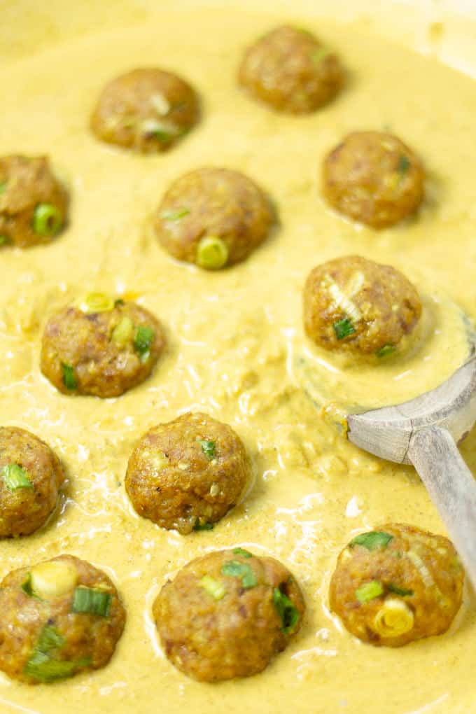Close up shot of coconut curry with pork meatballs being added to it