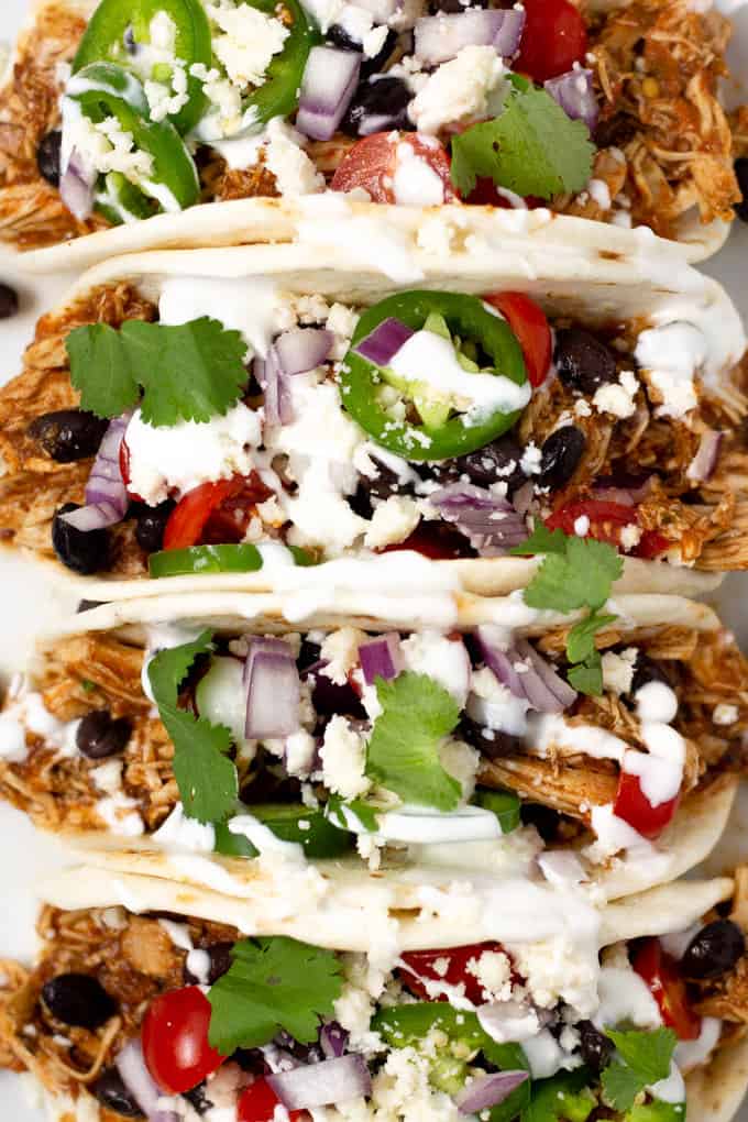 Overhead shot of 4 shredded chicken tacos garnished with diced red onion and fresh cilantro 