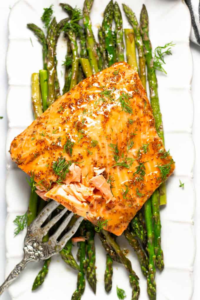 A large white platter filled with asparagus and sheet pan honey mustard salmon