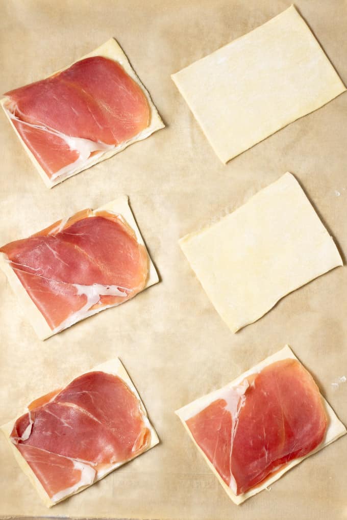 Parchment paper with 6 squares of puff pastry topped with prosciutto