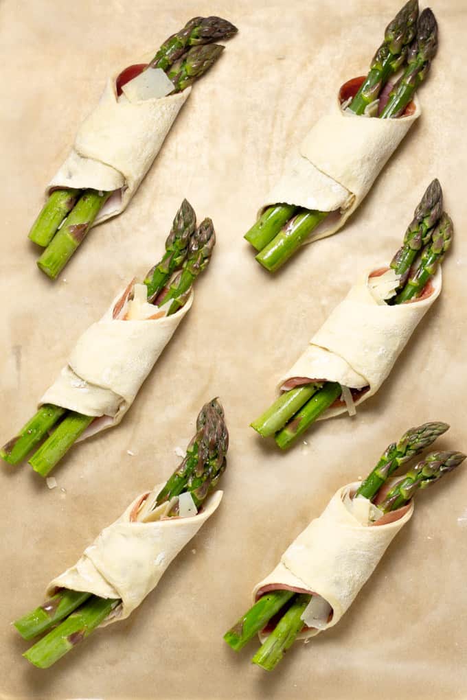 Parchment paper with 6 squares of puff pastry wrapped around prosciutto and asparagus
