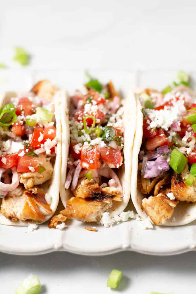 Close up shot of a three chicken tacos in flour tortillas garnished with fresh pico de gallo