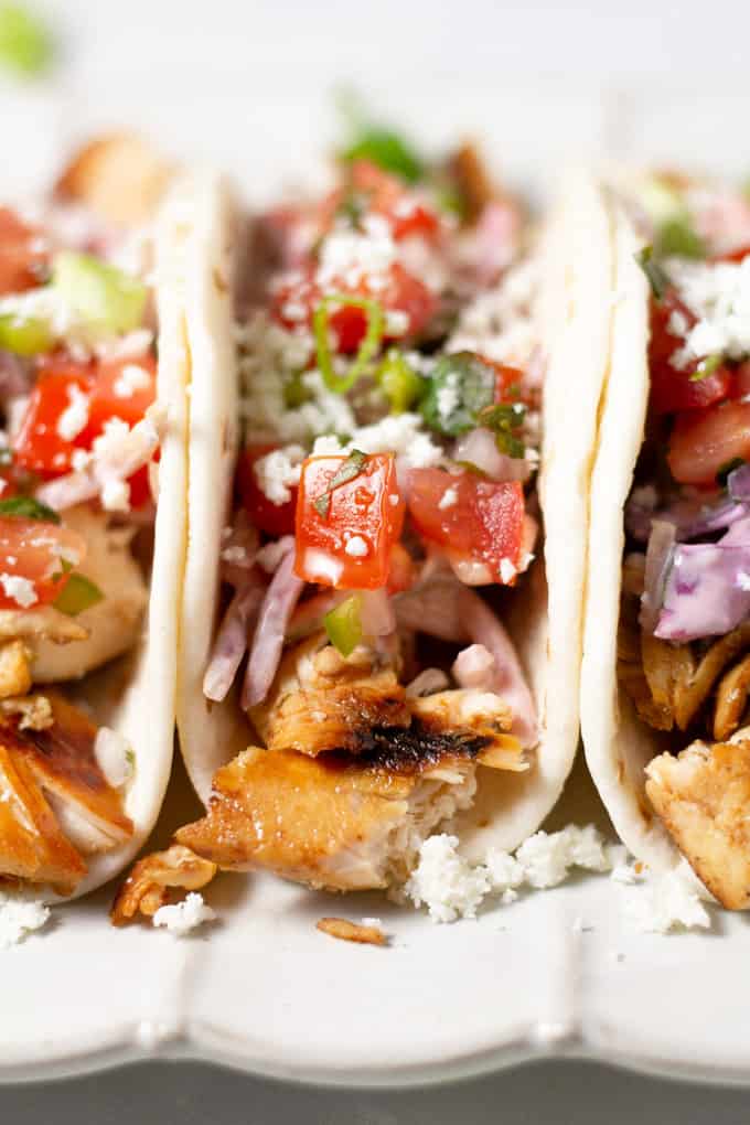 Close up shot of a three chicken tacos in flour tortillas garnished with fresh pico de gallo 