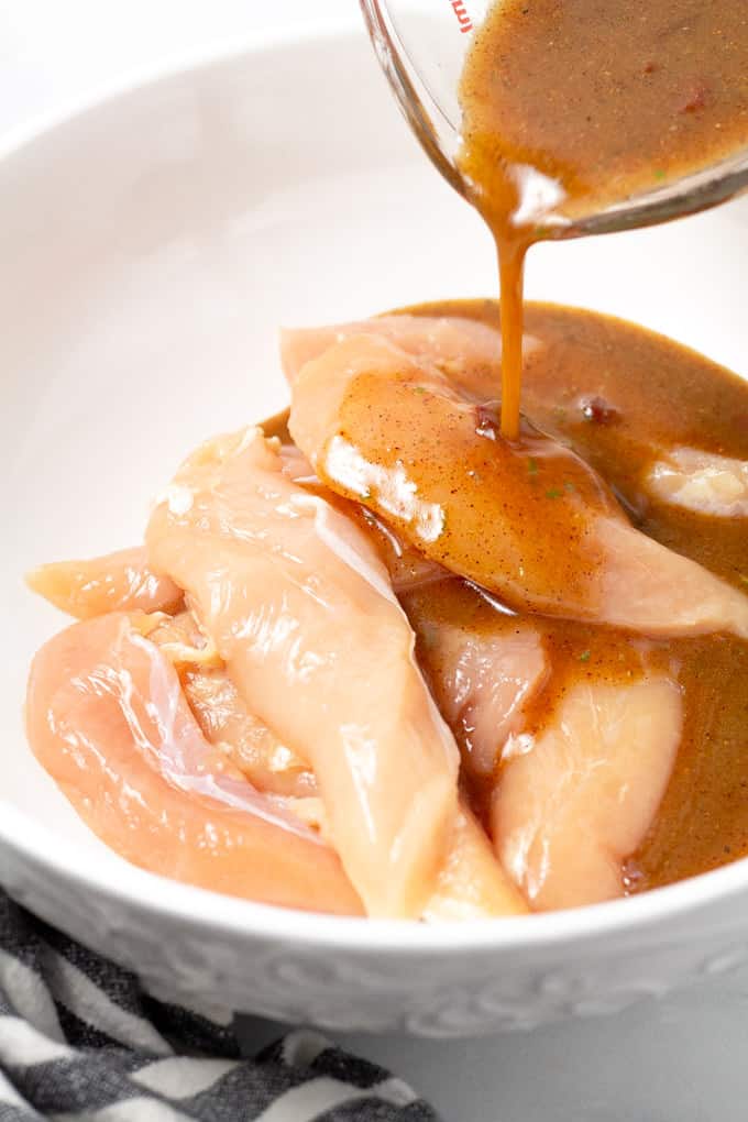 Close up shot of marinade being poured over chicken breast in a white bowl 