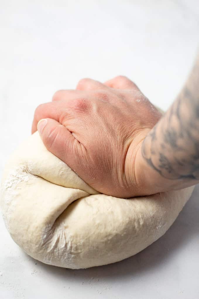 A white counter top with a ball of dough being kneaded by hand