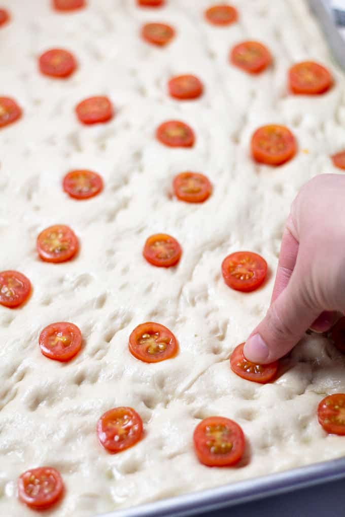 Tomatoes being pressed into the surface of focaccia bread in a pan 