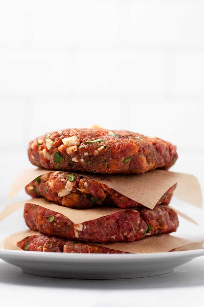Overhead shot of a stack of Mexican burgers on a white plate with parchment paper in between them