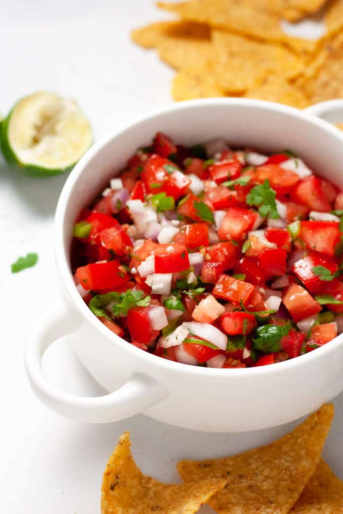 Close up shot of a white bowl filled with homemade pico de gallo surrounded by chips