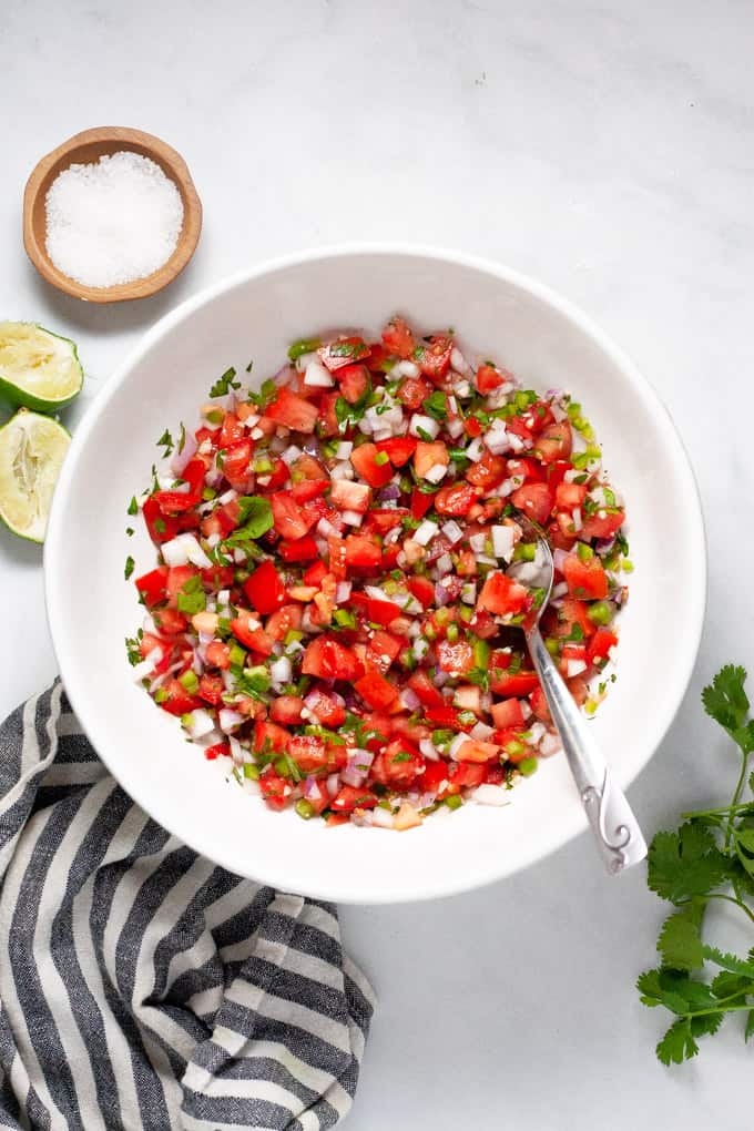 Overhead shot of a white bowl filled with homemade pico de gallo surrounded by chips