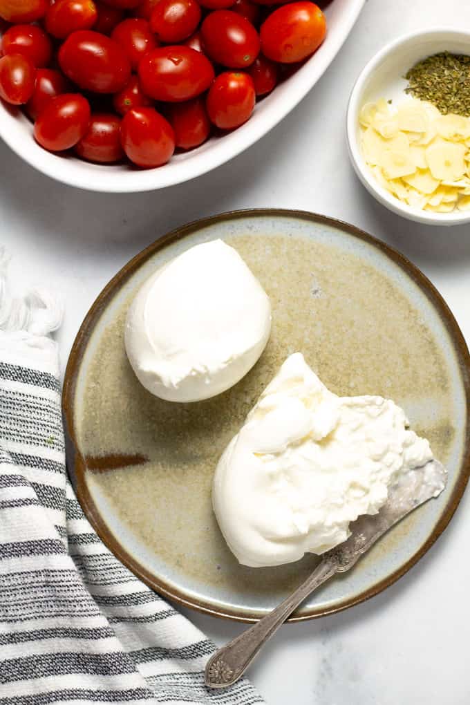 Close up shot of creamy burrata cheese on a gray plate on a white counter top 