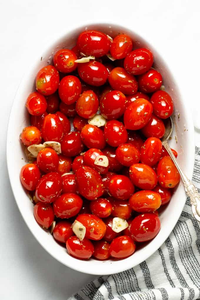 Overhead shot of a white oval baking dish filled with grape tomatoes tossed with olive oil, garlic and oregano