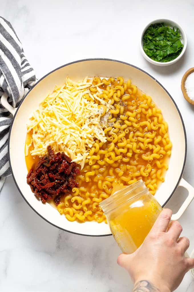 Overhead shot of a hand pour vegetable broth into a pan of one pot pasta