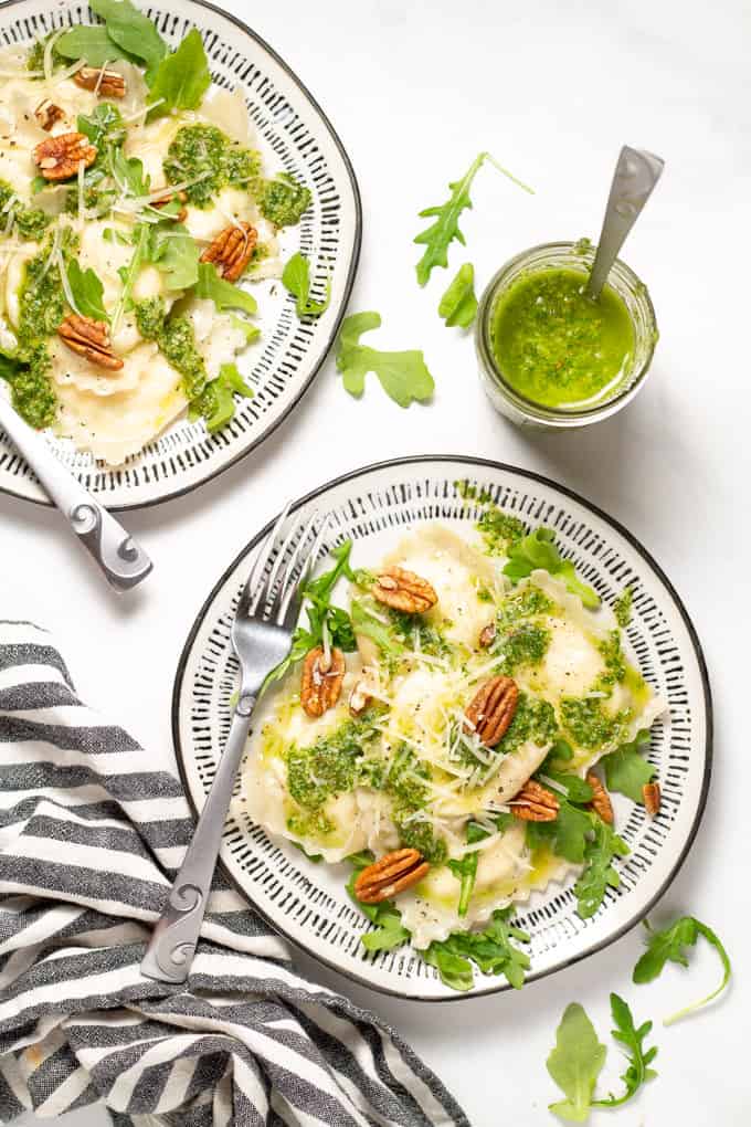 Overhead shot of two white plates filled with wonton ravioli and arugula pesto