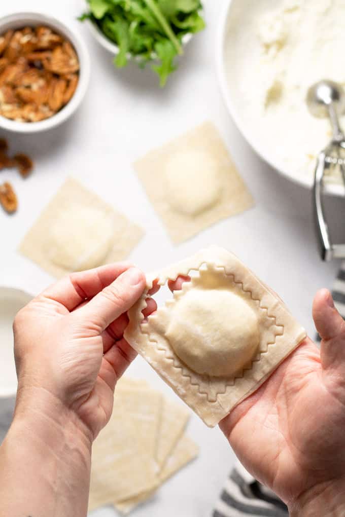 Overhead shot of a wonton ravioli after being stamped with a hand removing the excess wonton wrapper