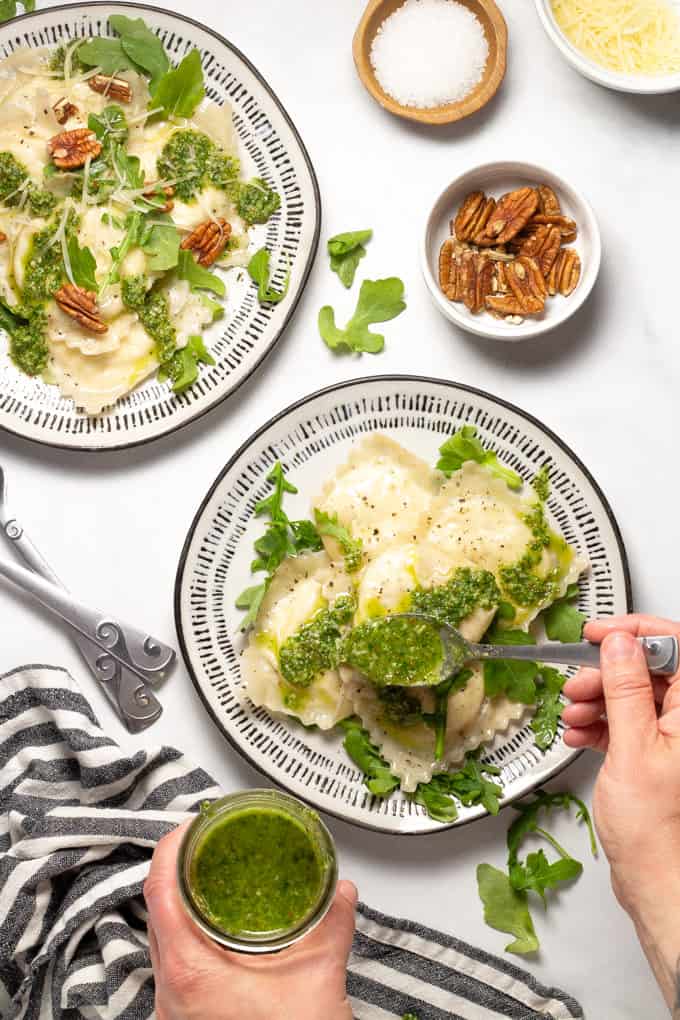 Overhead shot of two white plates filled with wonton ravioli and arugula pesto being spooned over it